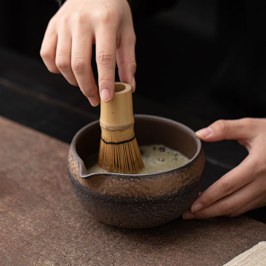 Hands whisking bright green matcha in dark Jian ware chawan bowl