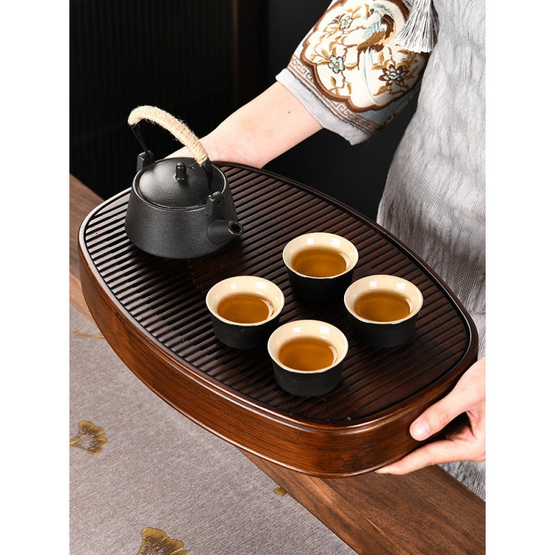 Dark bamboo tea tray holding ceramic teapot and two cups on linen surface