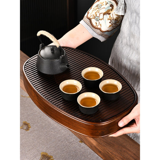 Dark bamboo tea tray holding ceramic teapot and two cups on linen surface